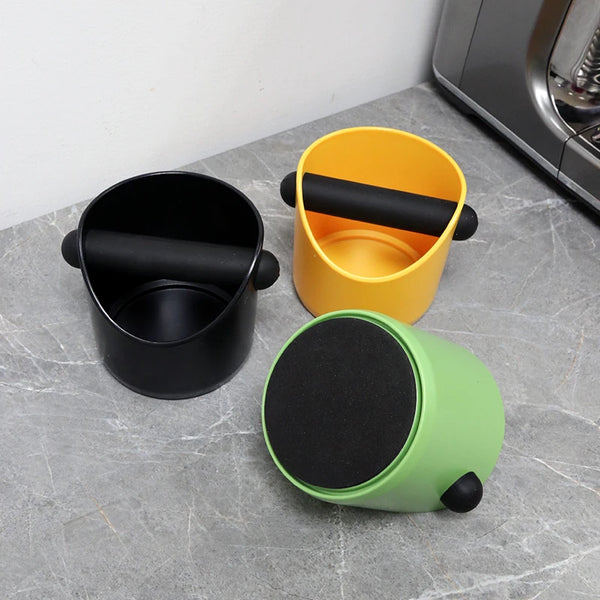 Three coffee grounds containers in black, yellow, and green sitting on a gray surface.