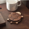 A set of solid wood turtle insulation mats and coasters resting on a dark wooden surface next to a white mug.