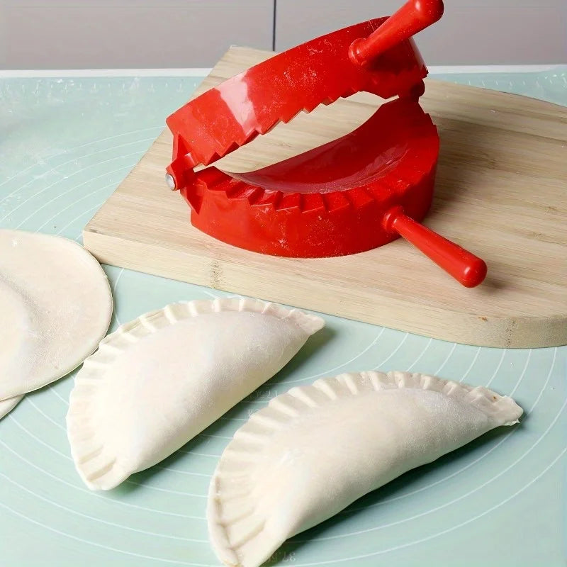 A red manual dumpling press is shown with two white pastry wrappers on a light green cutting board.
