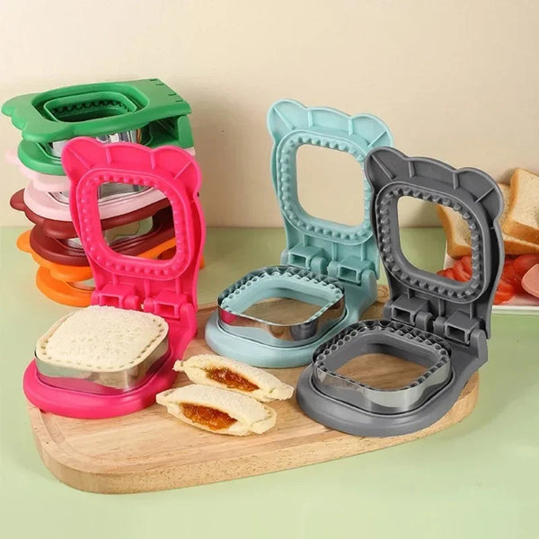 Ein Set aus fünf Plastik-Sandwich-Cuttern in verschiedenen Farben, darunter rosa, grün und grau, auf einem Holzbrett.