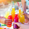 Hands hold colorful juice drinks in glass bottles with reusable plastic straws and cleaning brushes