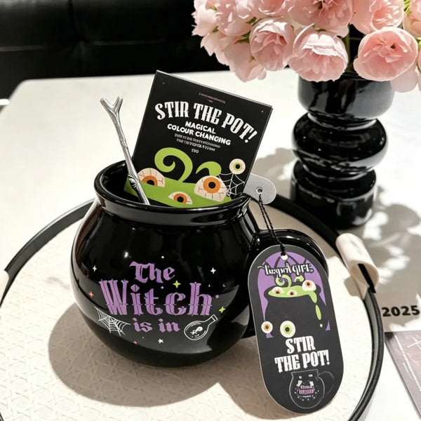 A black cauldron mug with a lid and a sign reading Stir the Pot featuring a witch theme.