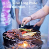 A hand holds a digital meat thermometer with a long probe over grilled meat on a barbecue grill.