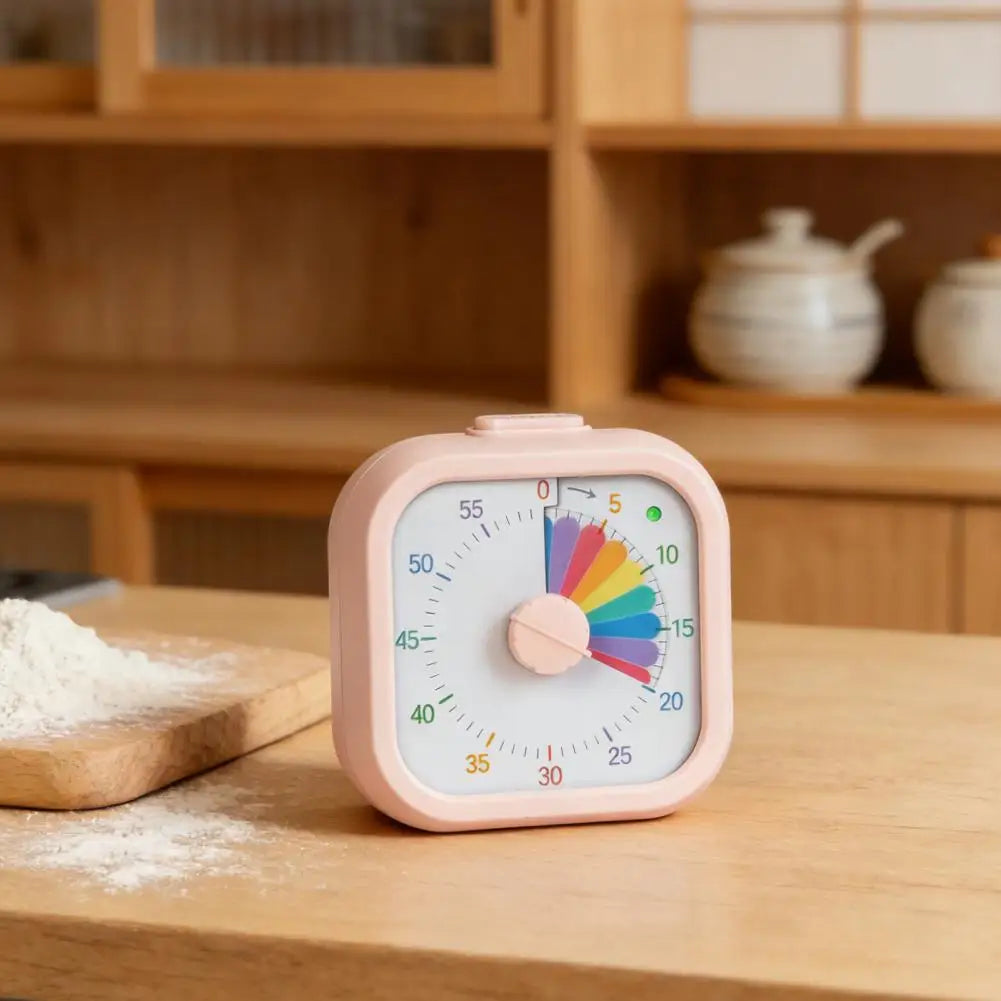 A pink visual timer for kids showing a colorful rainbow arc on a dial, resting on a wooden surface.
