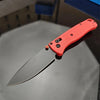 An orange folding utility knife with a silver blade is shown resting on a dark surface.