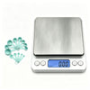 A silver digital kitchen scale with a blue display and multiple measuring cups shown next to it.
