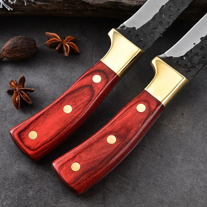 A set of three forged boning stainless steel kitchen knives with red wooden handles and gold accents resting on a dark surfac