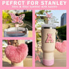 A pink tumbler with an 'A' design, featuring a handle and a butterfly charm.