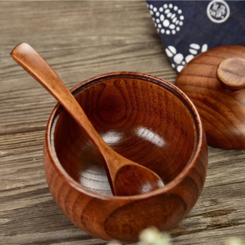 A wooden salt and spice shaker set featuring a small wooden bowl and a wooden spoon on a rustic wooden surface.