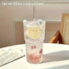 A clear glass drinking cup filled with pink liquid, featuring a lid and a straw.