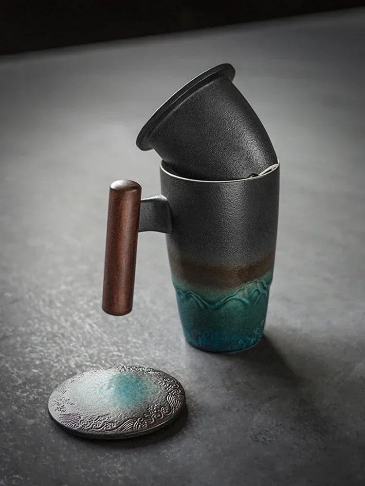 Una taza de té de cerámica oscura con tapa y asa de madera junto a un posavasos de cerámica a juego.