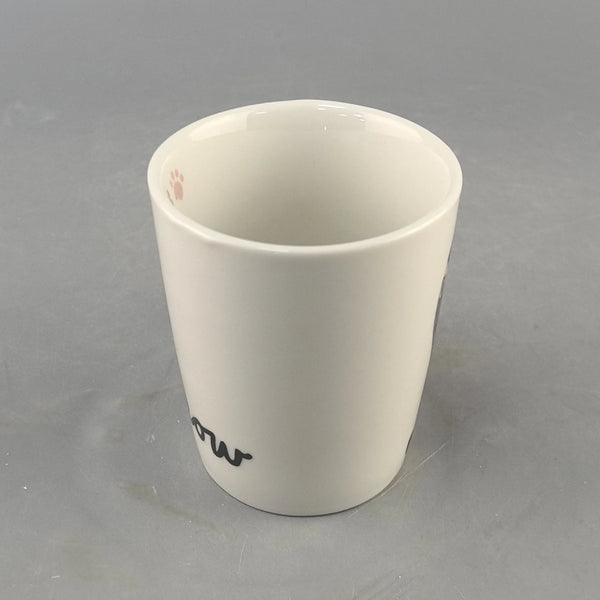 Weiße Keramiktasse mit kleiner Pfotenspur und stilisierten Initialen auf der Seite.