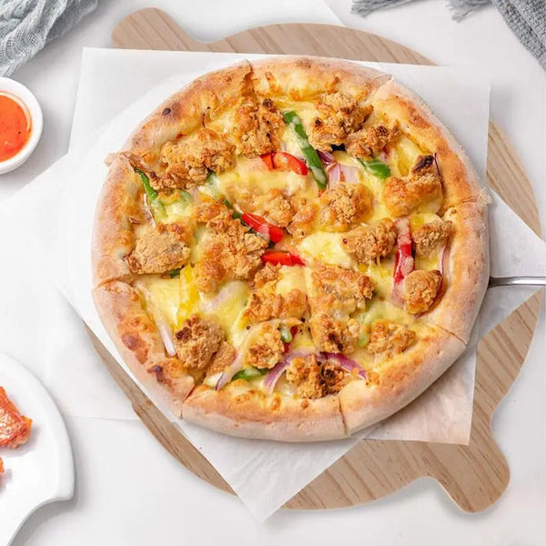 Runde Pizza mit Käse und knusprigen Fleischstücken auf einem Holzbrett mit Backpapier.