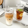 A tall glass of iced tea or beverage with a clear lid and straw sits on a white surface next to a stack of books.