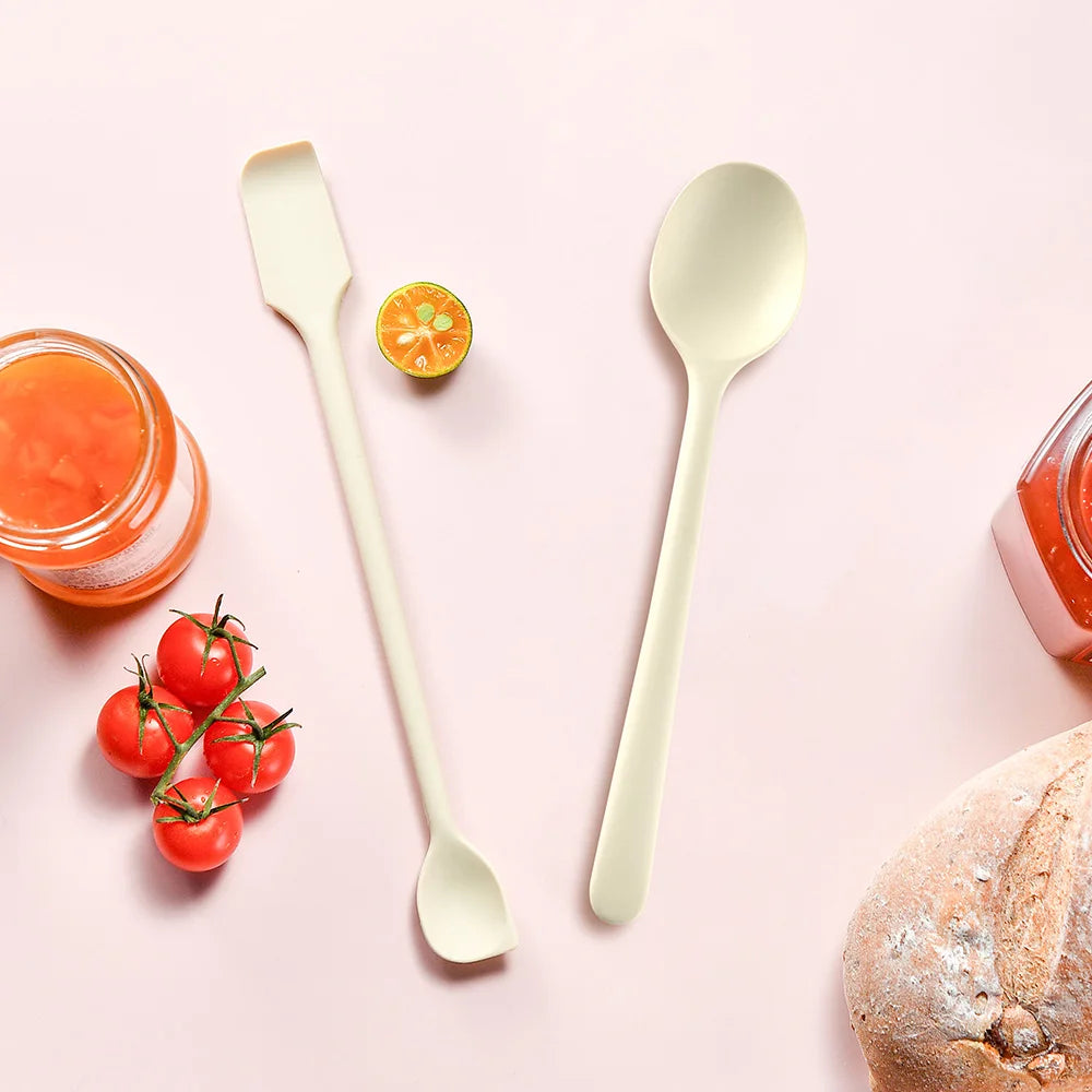 A set of silicone heat resistant spoons used for serving jam and rice, placed on a pink background with fresh fruit and bread