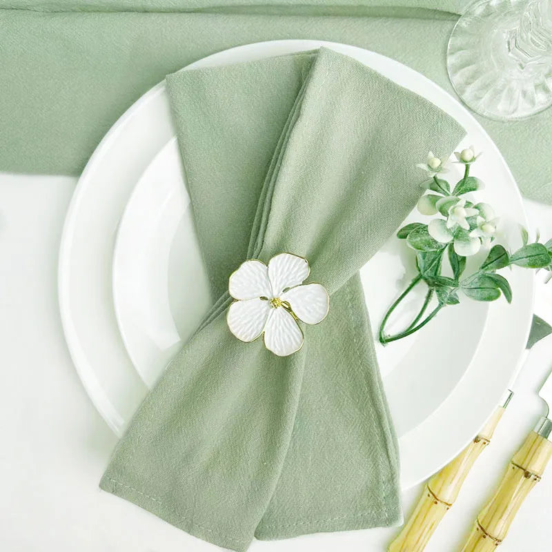 A set of reusable sage green cotton cloth napkins folded and placed on a white plate with a glass.