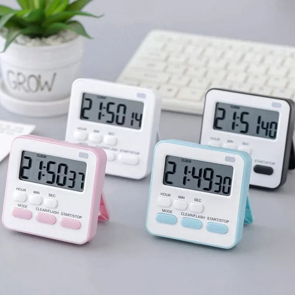 Eine Sammlung rosa und hellblaue digitale Küchentimer auf einer grauen Oberfläche neben einer weißen Tastatur.