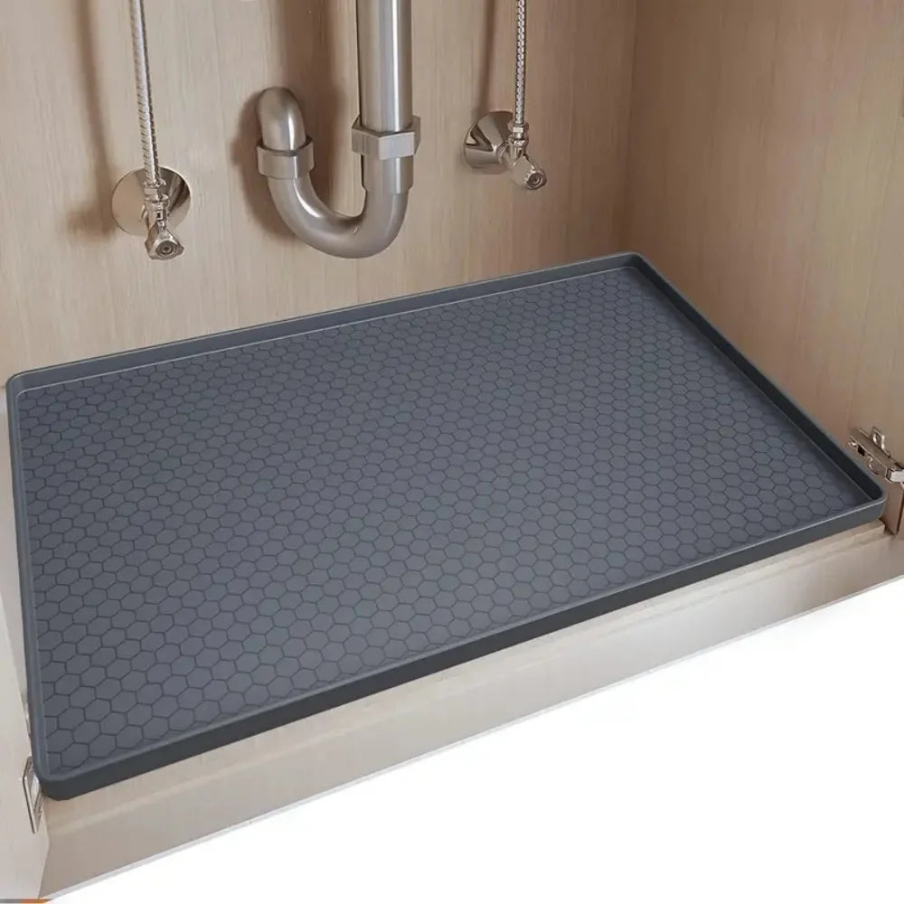A silicone under sink drain tray with a hexagonal pattern is installed in a cabinet, featuring metal plumbing fixtures above.