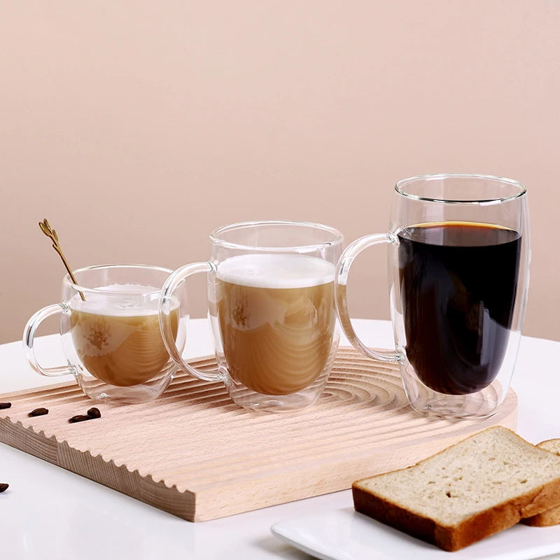 Three heat resistant double wall glass drinking cups filled with coffee or tea on a wooden board.