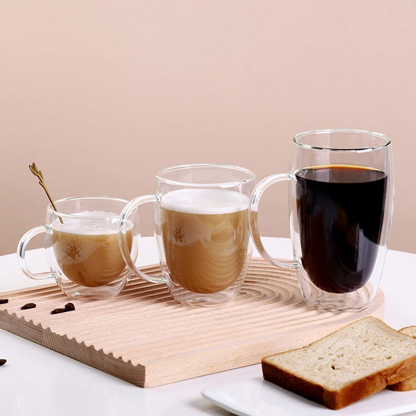Drei hitzebeständige doppelwandige Glasbecher, gefüllt mit Kaffee oder Tee, auf einem Holzbrett.