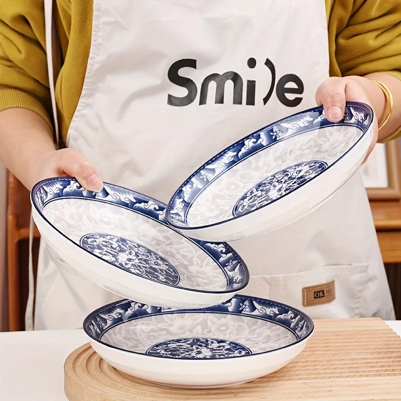 Un jeu de deux élégantes assiettes de porcelaine bleu et blanc tenues par une personne en tablier blanc.