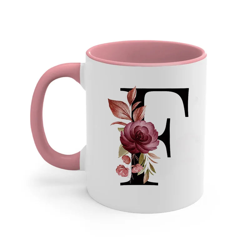 A pink coffee mug with a large black letter T monogram featuring a cluster of deep red and pink roses.