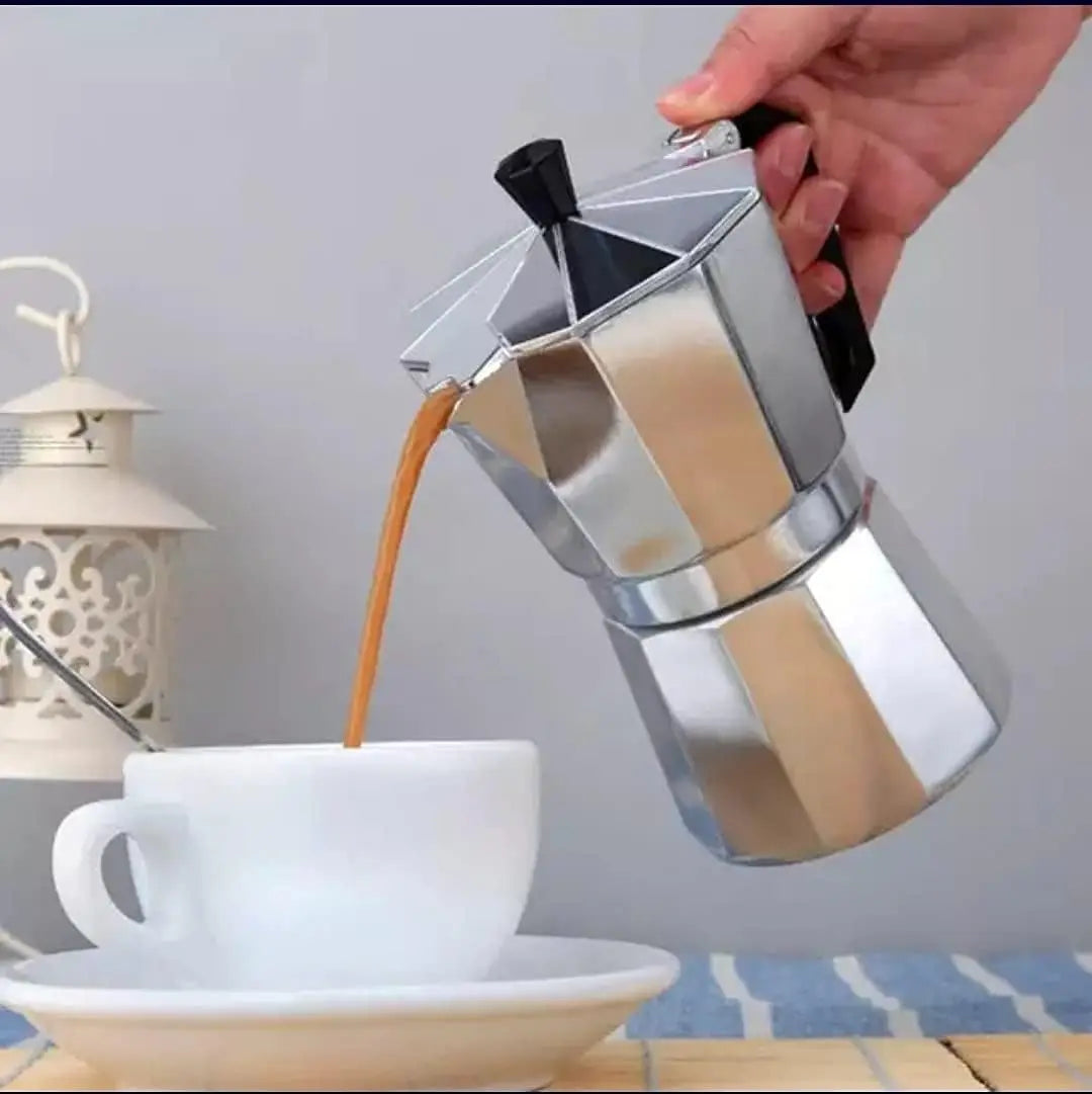 A hand pours coffee from a silver moka pot into a white cup.