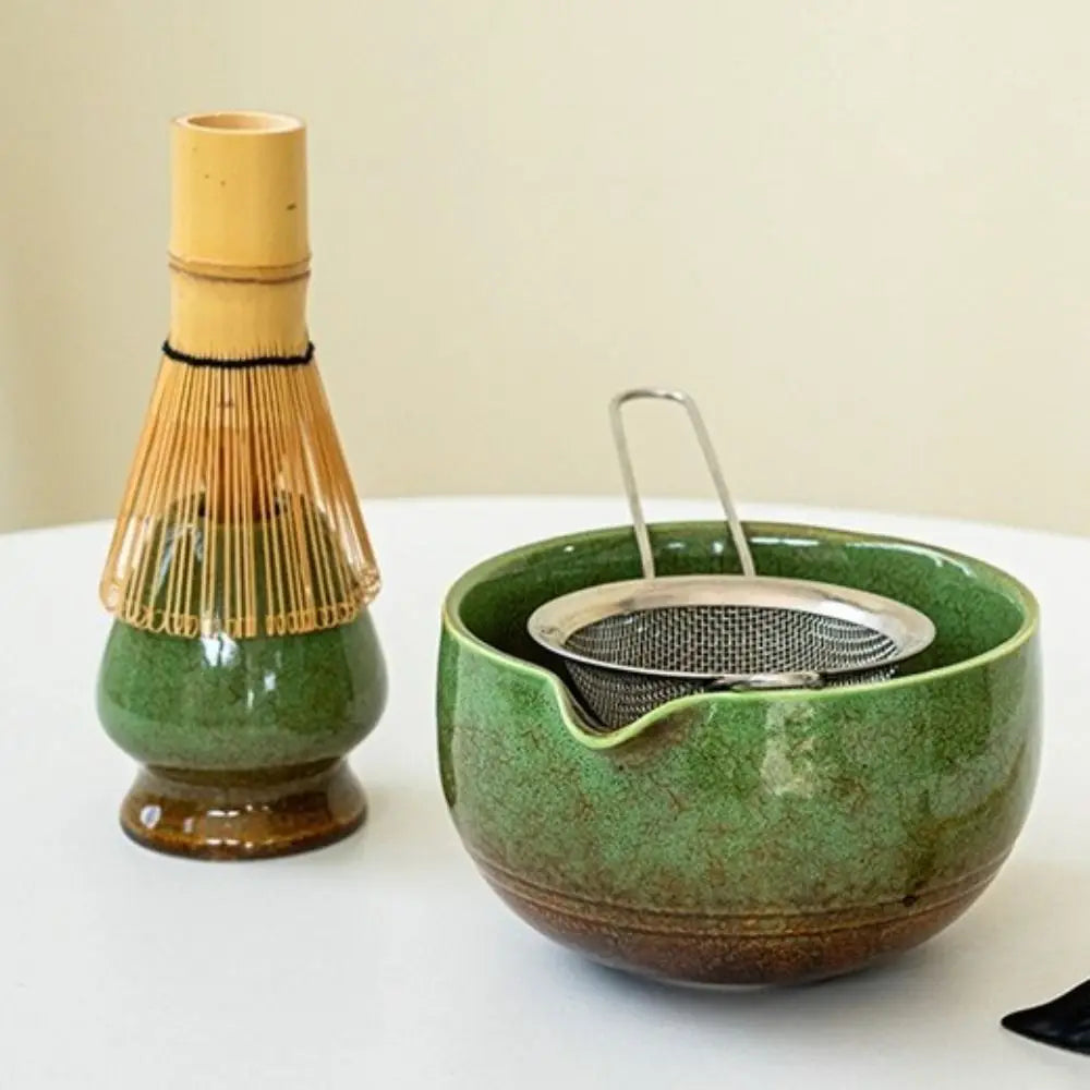 A traditional Japanese matcha tea set featuring a ceramic green bowl and a bamboo whisk.