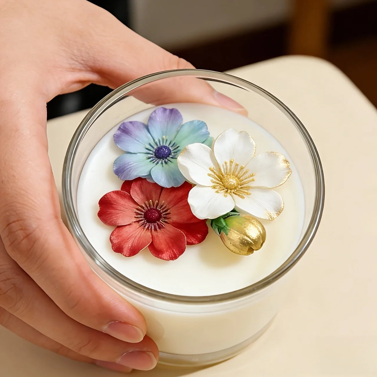 A hand holds a clear glass bowl filled with white silicone flower molds for baking, featuring purple, blue, and red blossoms.