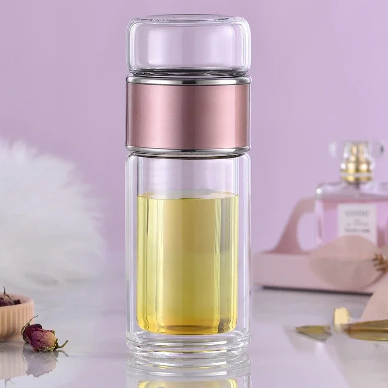A double-layer borosilicate glass tea infuser with a pink band and yellow liquid inside.