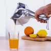 A hand is using a heavy-duty metal citrus juicer to extract juice from a lemon and pour it into a glass.