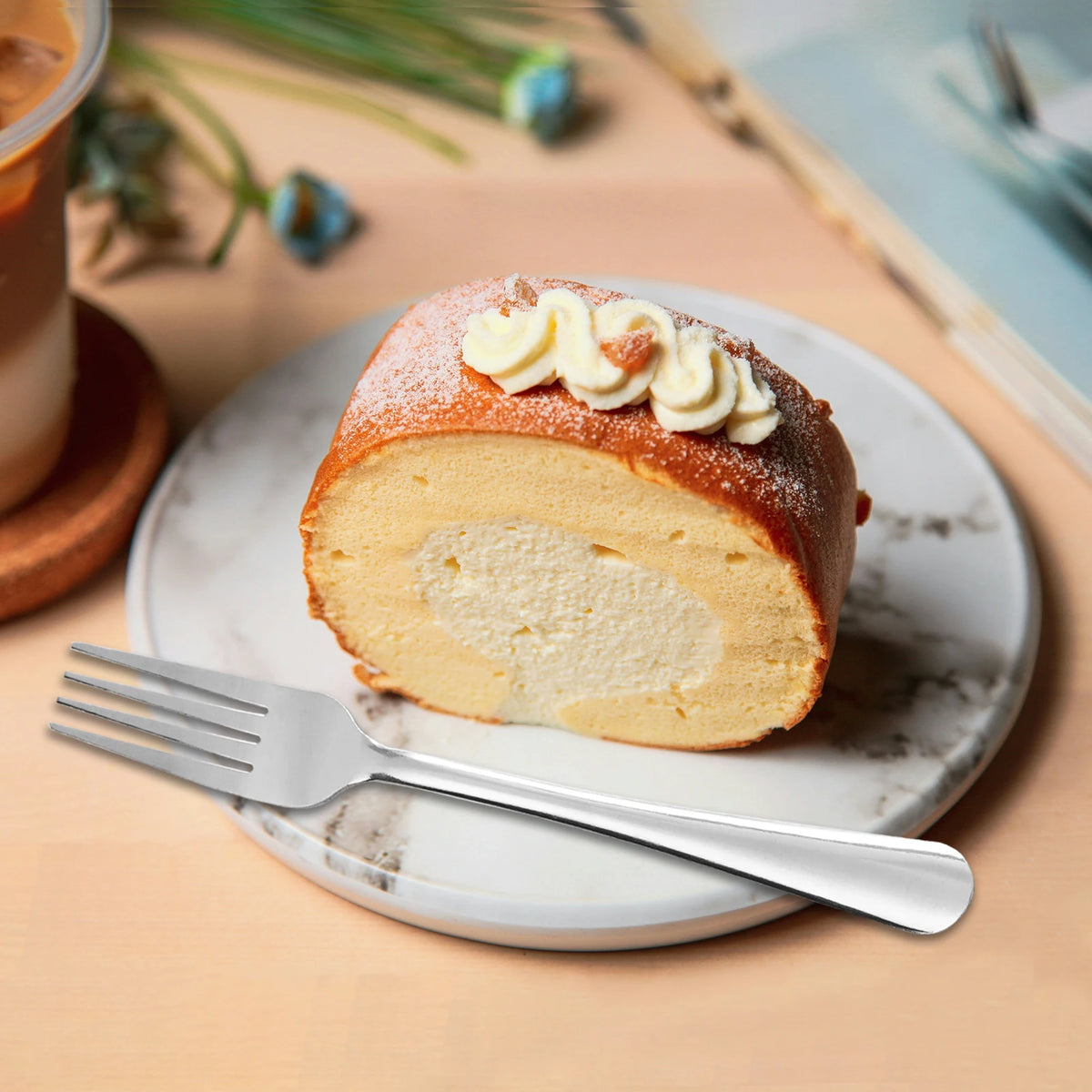 A sliced sweet loaf cake dusted with powdered sugar and topped with cream on a white plate next to a stainless steel fork.
