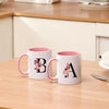 A white coffee mug with a pink interior and a black floral monogram on the side.