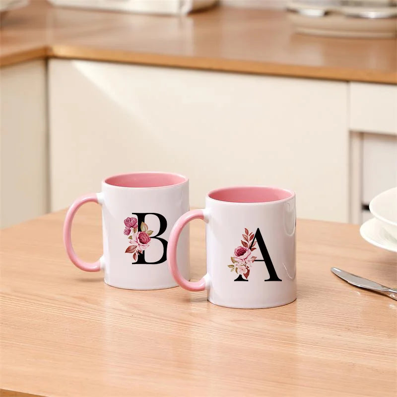 A white coffee mug with a pink interior and a black floral monogram on the side.