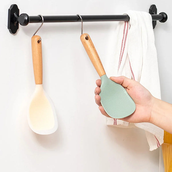 Eine Hand hält einen Silikonspatel mit einem Holzgriff, der an einer Leiste hängt, neben einem weißen Handtuch.