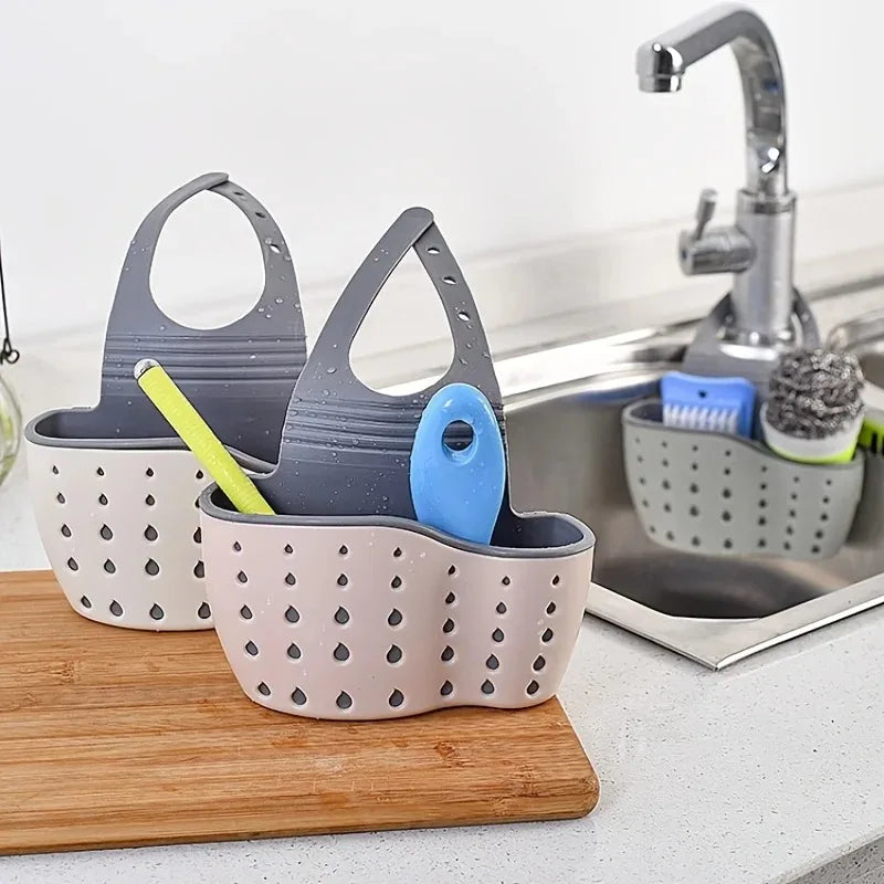 A pink and gray adjustable sink drain hanging sponge rack with silicone tools and sponges placed on a wooden cutting board.