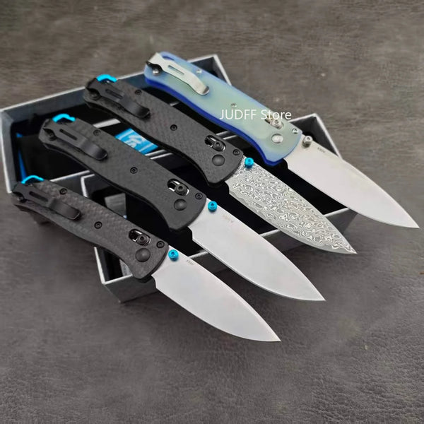 A set of four folding outdoor pocket knives with black and blue handles and silver blades are displayed in a dark box.