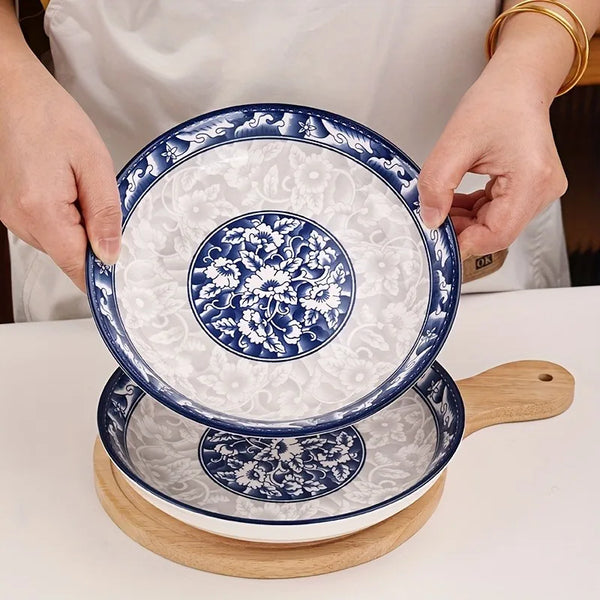 Ein Set aus zwei eleganten blau-weißen Porzellan-Dinnerplatten wird von Händen auf einem Holzservierbrett gehalten.
