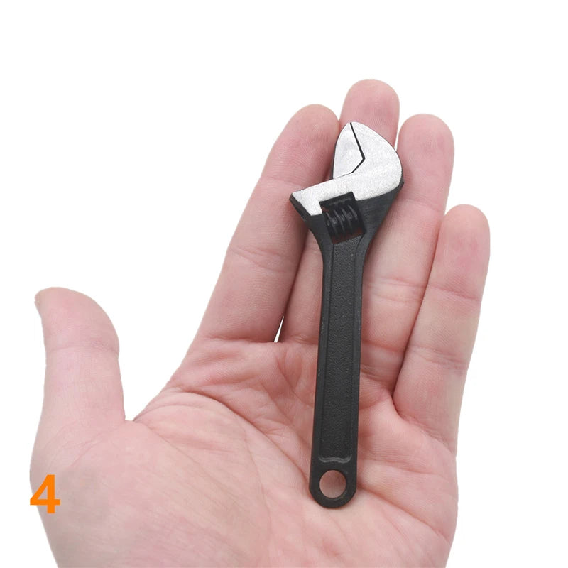 A hand is holding a small, silver and black compact mini adjustable spanner wrench.
