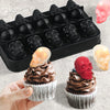 A black silicone mold tray filled with skull-shaped ice cube molds and a hand holding a cupcake with a red skull topping.