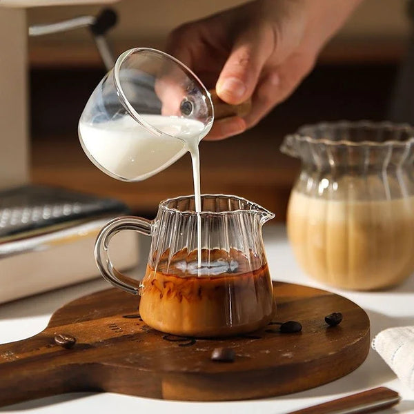 Eine Hand gießt Milch aus einem Glas in eine Milchkanne für Tee oder Espresso.