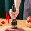 A hand holds a black meat tenderizer tool over a piece of raw red meat on a wooden cutting board.