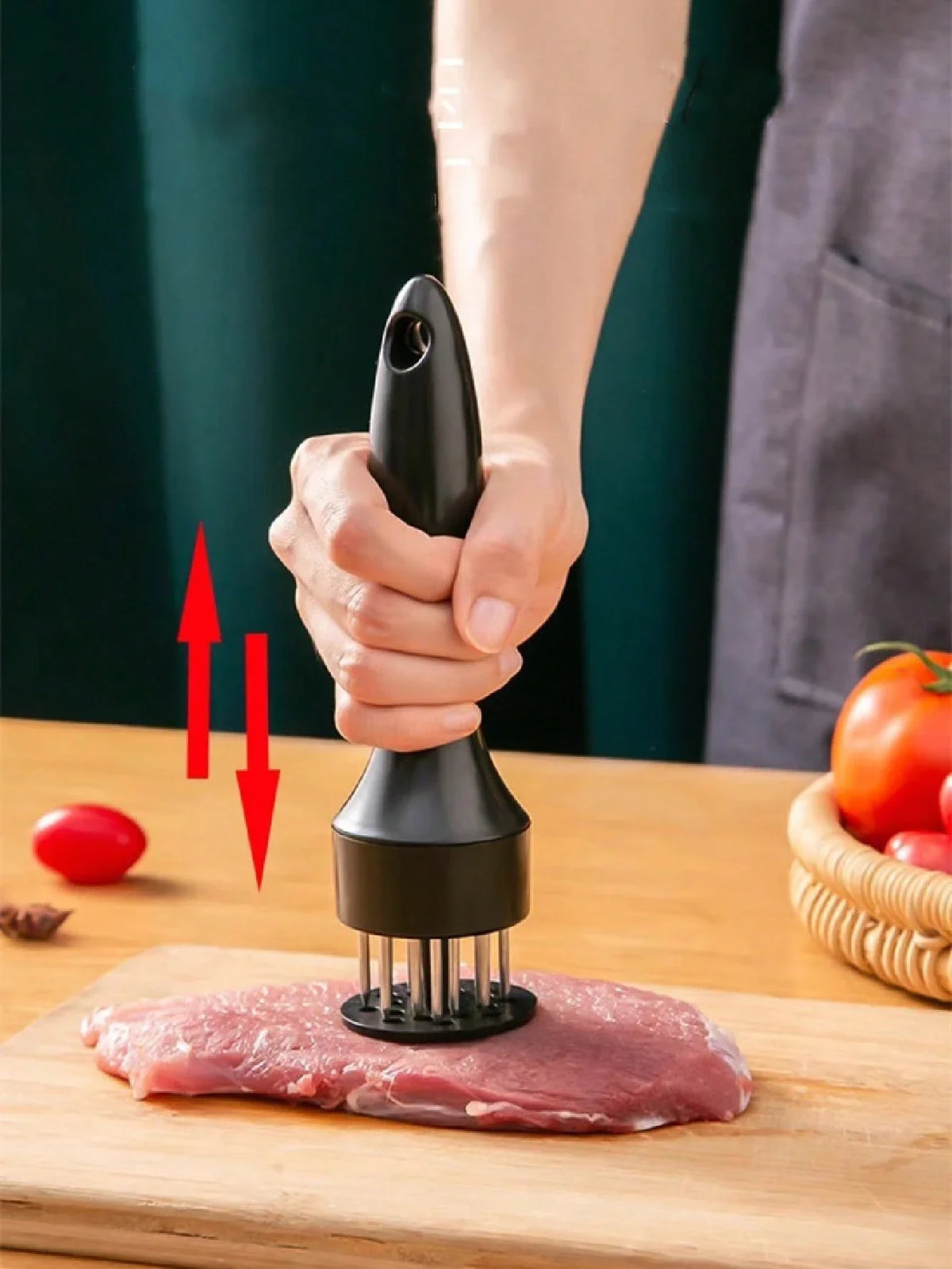 A hand holds a black meat tenderizer tool over a piece of raw red meat on a wooden cutting board.