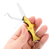 A hand holds a gold-colored stainless steel keychain tool shaped like a fish with scissors.