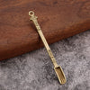 A brass metal mini shovel spoon with a decorative handle rests on a dark wooden surface.