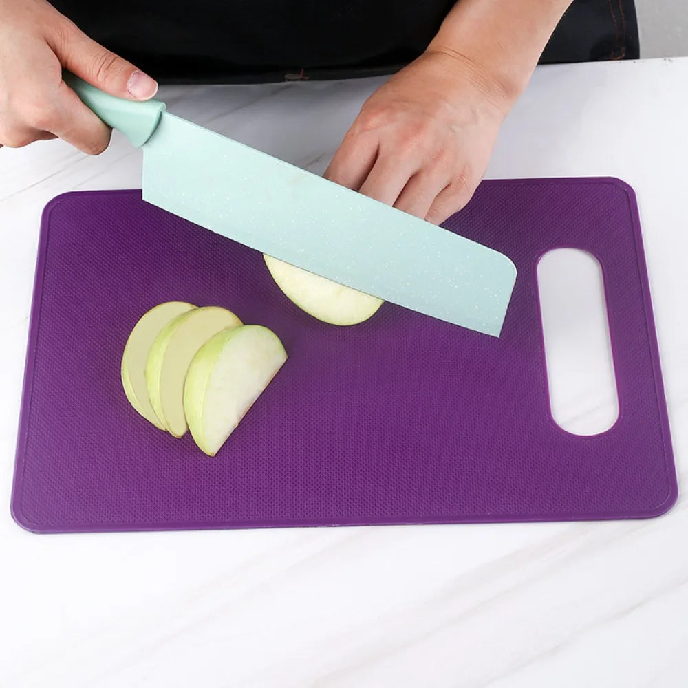A hand is using a light green plastic knife to cut an apple on a purple cutting board.