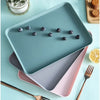 A teal plastic serving tray holds dark purple berries and is accompanied by a pink serving platter and wooden utensils.