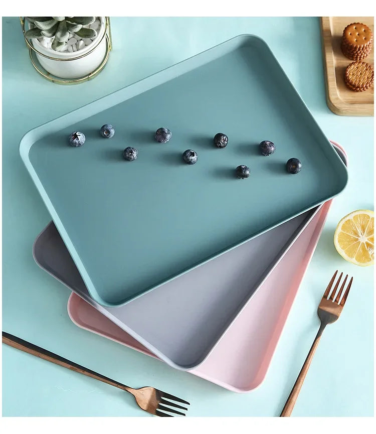 A teal plastic serving tray holds dark purple berries and is accompanied by a pink serving platter and wooden utensils.