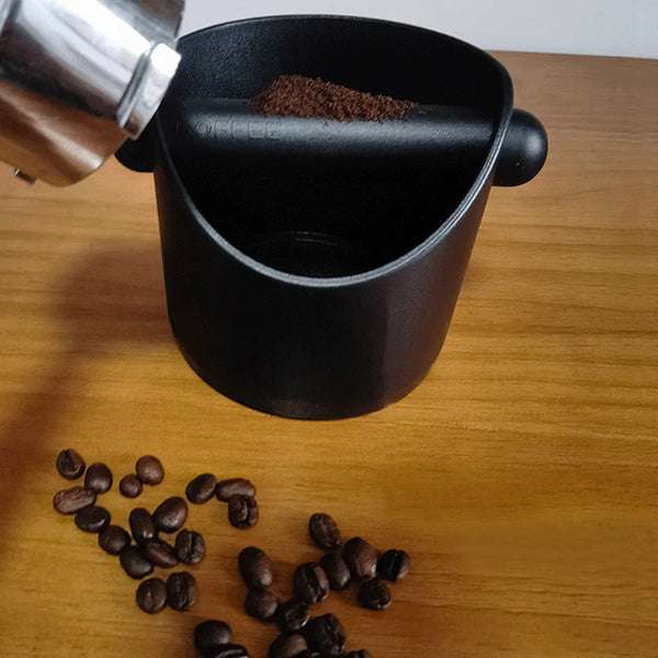 Schwarze Espressoknoche gefüllt mit Kaffeemehl, neben losen Kaffeebohnen auf einer Holzoberfläche.