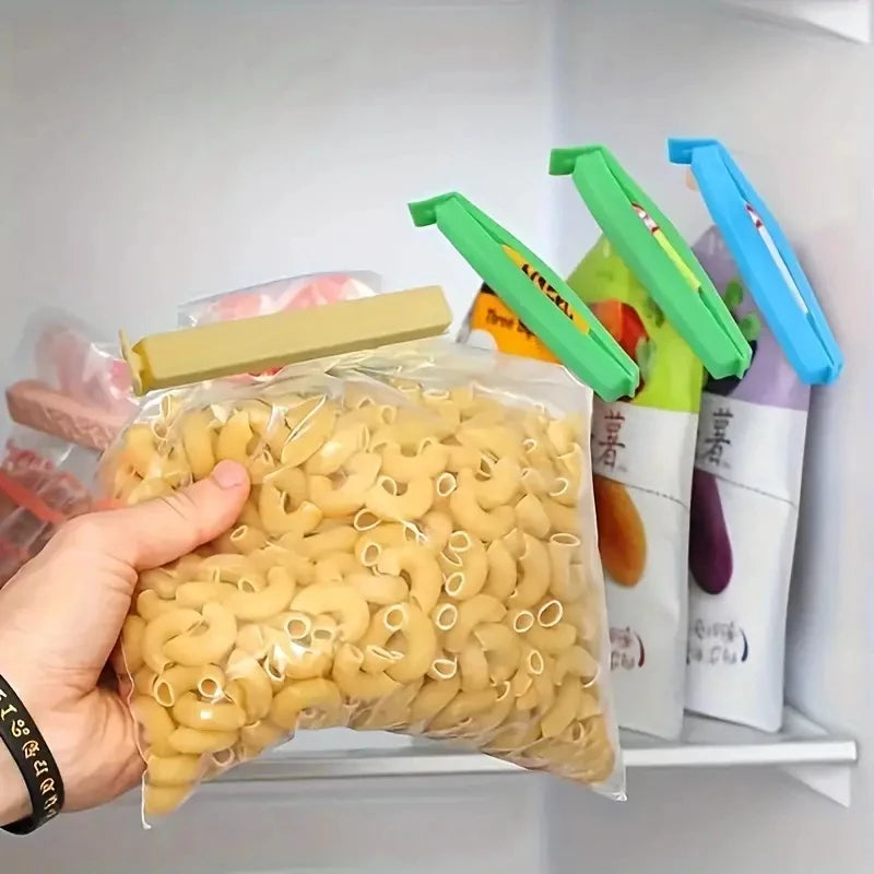 A hand holds a clear bag filled with light yellow popcorn kernels next to colorful reusable sealing clips.